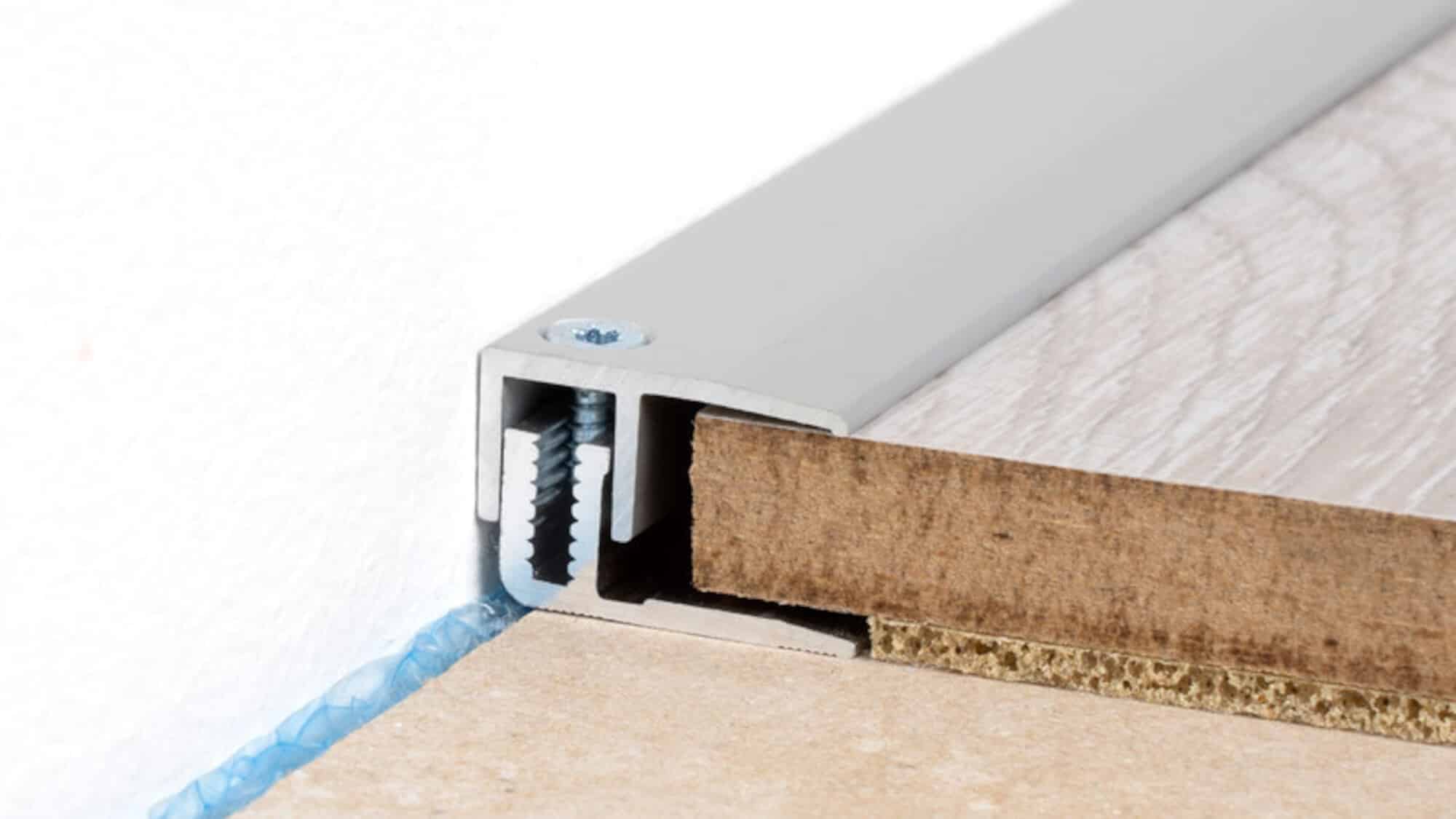 Detailaufnahme eines Aluminiumprofilabschlusses, das den Übergang zwischen zwei Bodenbelägen zeigt, mit sichtbarem Holz und einem Schraubengewinde.