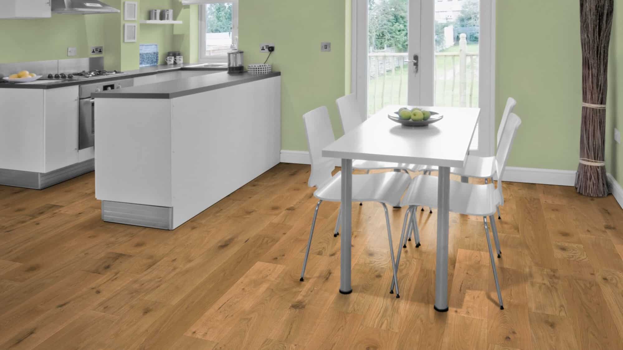 Moderne Küche mit hellgrünen Wänden, einem weißen Küchenschrank und einem Tisch mit vier weißen Stühlen. Auf dem Tisch befindet sich eine Schale mit Äpfeln. Der Boden ist aus hellem Holz.