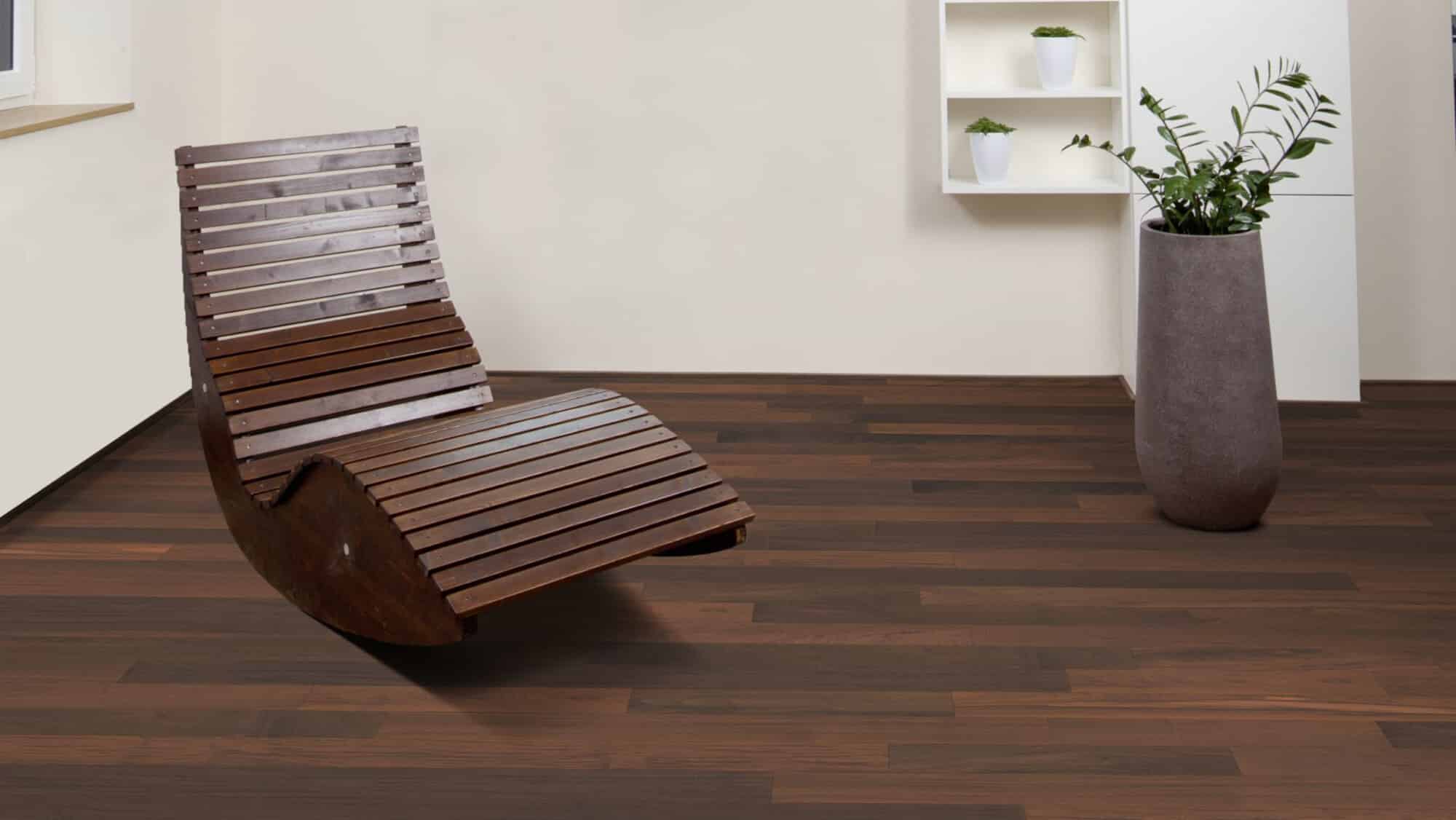 Ein moderner, geschwungener Holzstuhl steht auf einem dunklen Holzboden. Im Hintergrund befindet sich ein grauer Topf mit einer Pflanze und ein Regal mit weißen Töpfen. Die Wände sind in einem neutralen Farbton gehalten.
