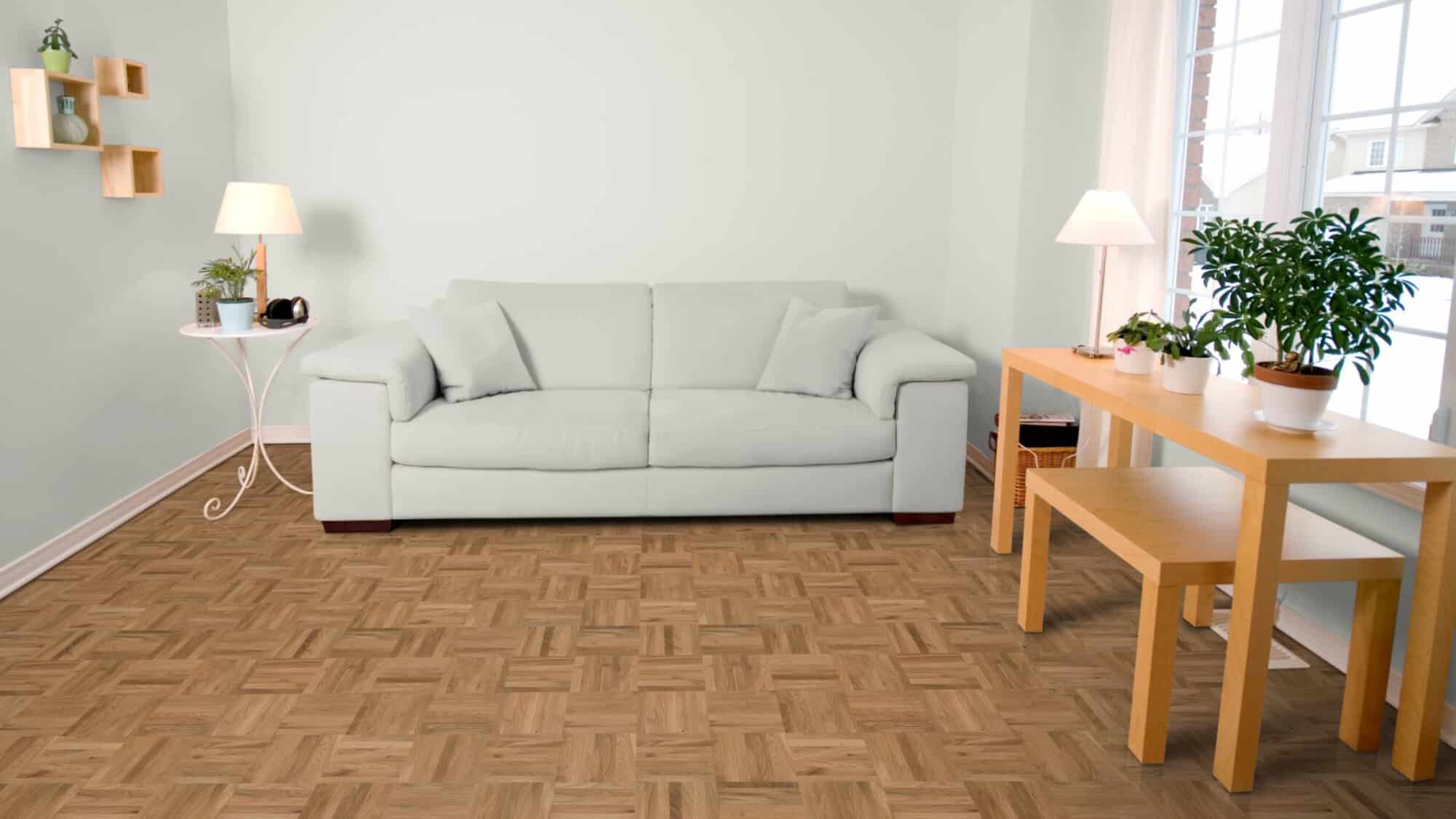 Heller Wohnraum mit einem beigen Sofa, einem kleinen Tisch mit Pflanzen und einer Lampe. Der Boden ist aus Holz mit einem schachbrettartigen Muster, und große Fenster lassen viel Licht herein. An der Wand sind dekorative Regale angebracht.