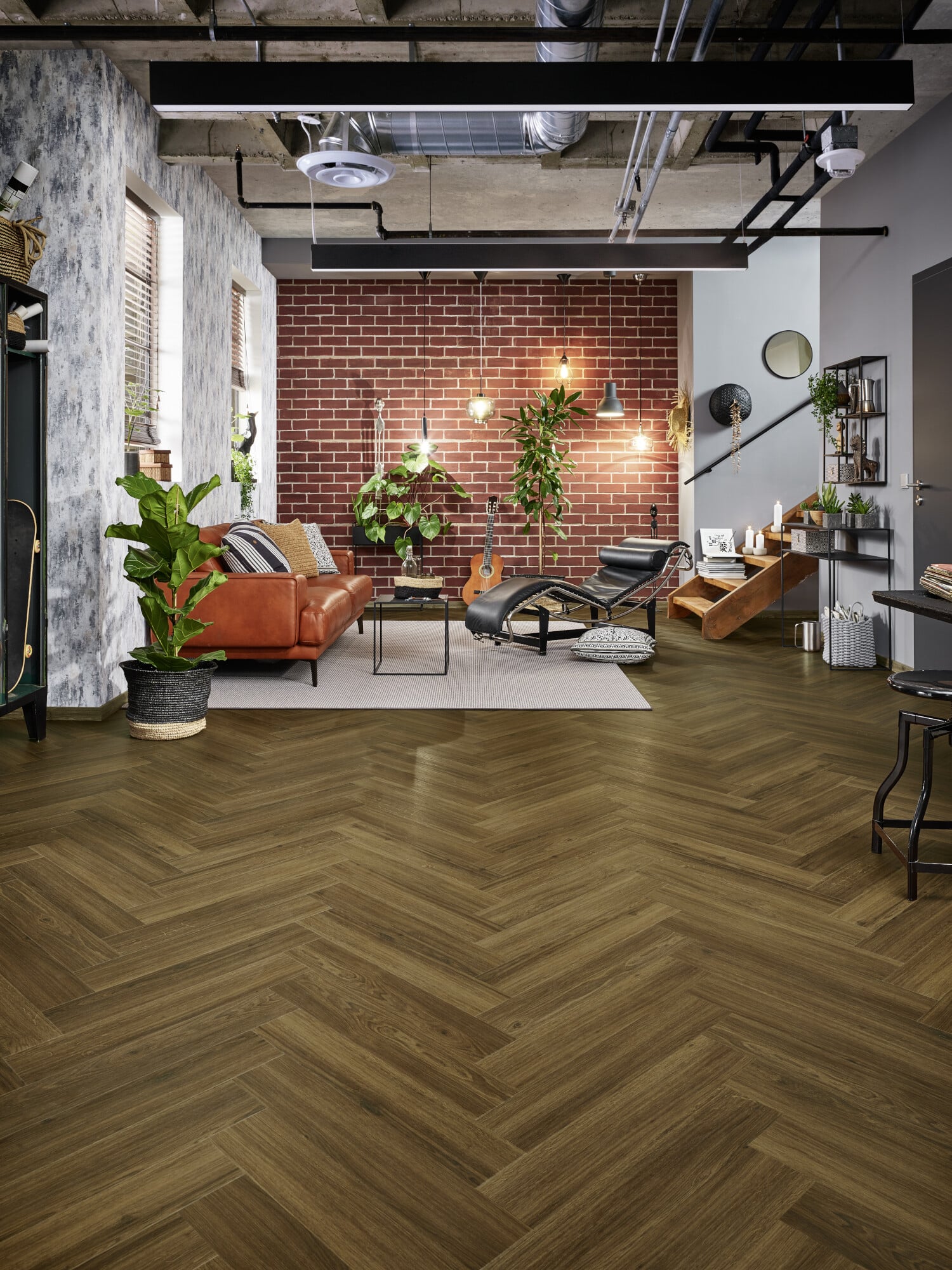 Ein modernes Wohnzimmer mit Holzfußboden in Fischgrätmuster, einer roten Ziegelwand und einem gemütlichen, orangefarbenen Sofa. Es gibt Pflanzen, eine Gitarre, verschiedene Beleuchtungselemente und stilvolle Möbel, die eine einladende Atmosphäre schaffen.