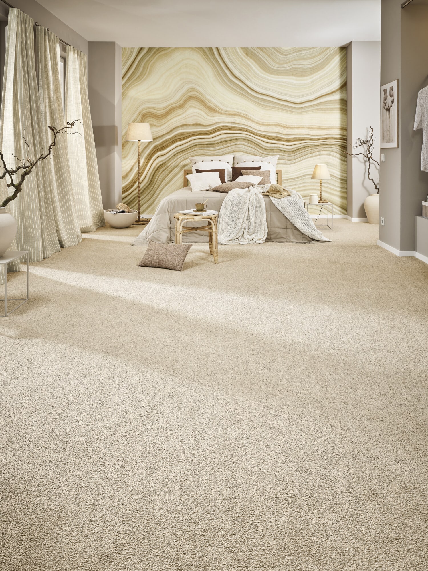 Ein modernes Schlafzimmer mit einem großen Bett, weichen Kissen und Decken in neutralen Farben. Die Wände sind in sanften Erdtönen gehalten, mit einer auffälligen, wellenförmigen Tapete. Ein Teppich in hellem Beige bedeckt den Boden, und große Fenster mit hellen Vorhängen lassen viel Tageslicht herein. Eine stilvolle Stehlampe und dekorative Elemente wie ein kleiner Tisch und Kissen sorgen für eine gemütliche Atmosphäre.
