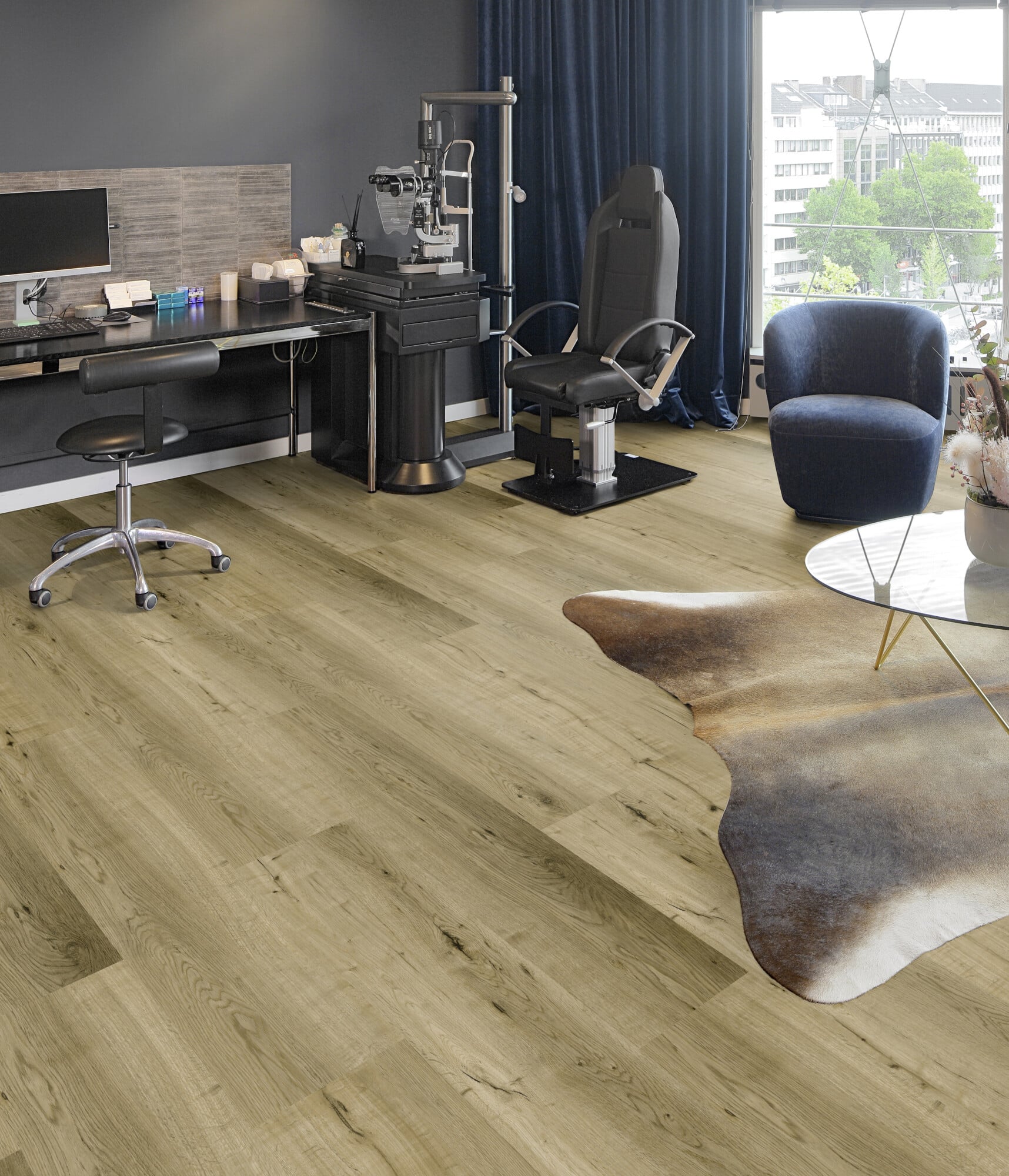 Ein modernes Arbeitszimmer mit einem Schreibtisch, einem ergonomischen Stuhl und einem Behandlungsstuhl. Der Raum hat einen Holzfußboden, einen großen Fensterblick und einen gemütlichen Sessel. Ein Teppich in Form von Tierfell liegt auf dem Boden.