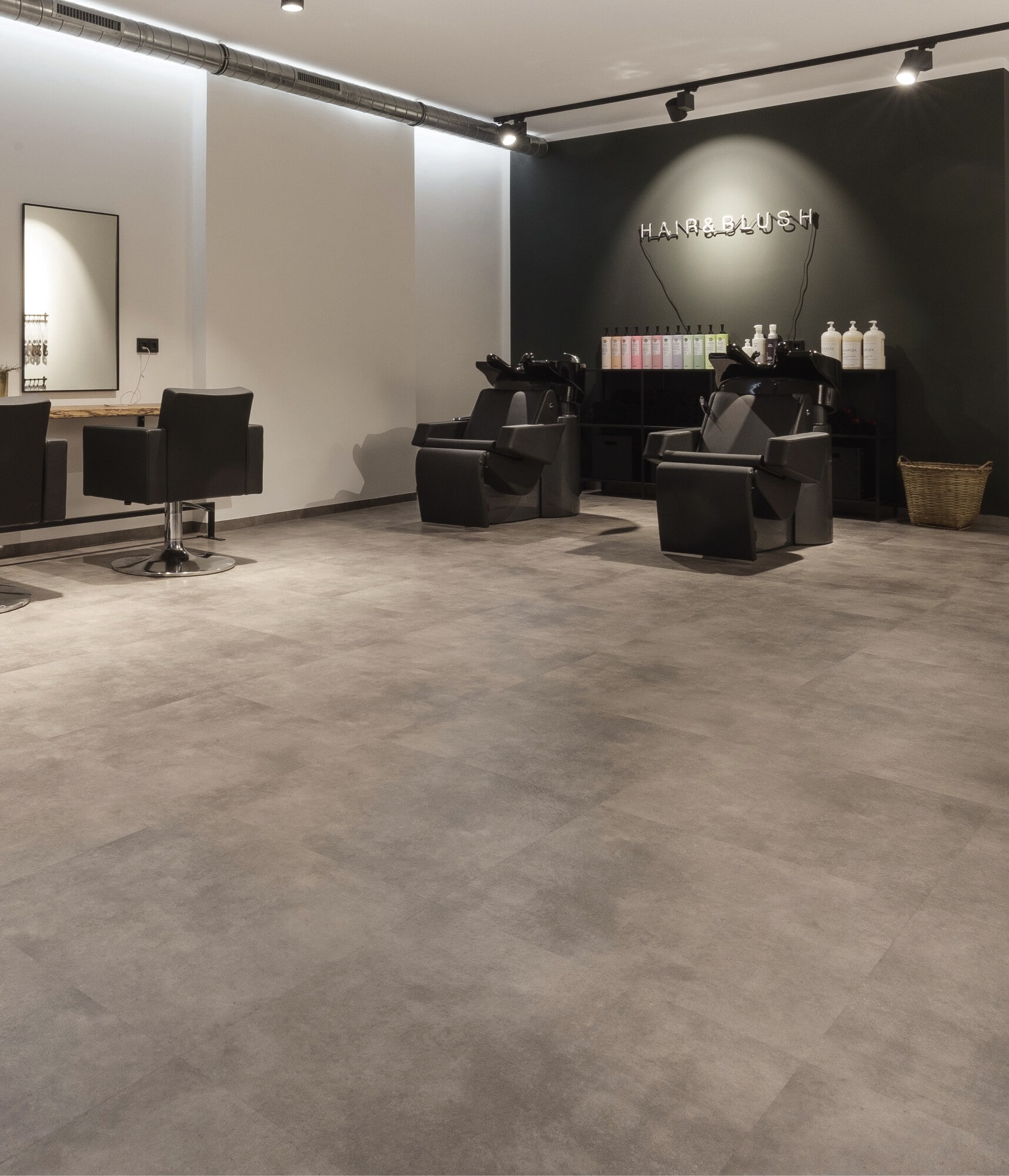 Ein moderner Friseursalon mit eleganten, schwarzen Stühlen und Waschbecken. Die Wände sind in neutralen Farben gehalten, und es gibt eine beleuchtete Wand mit dem Schriftzug 