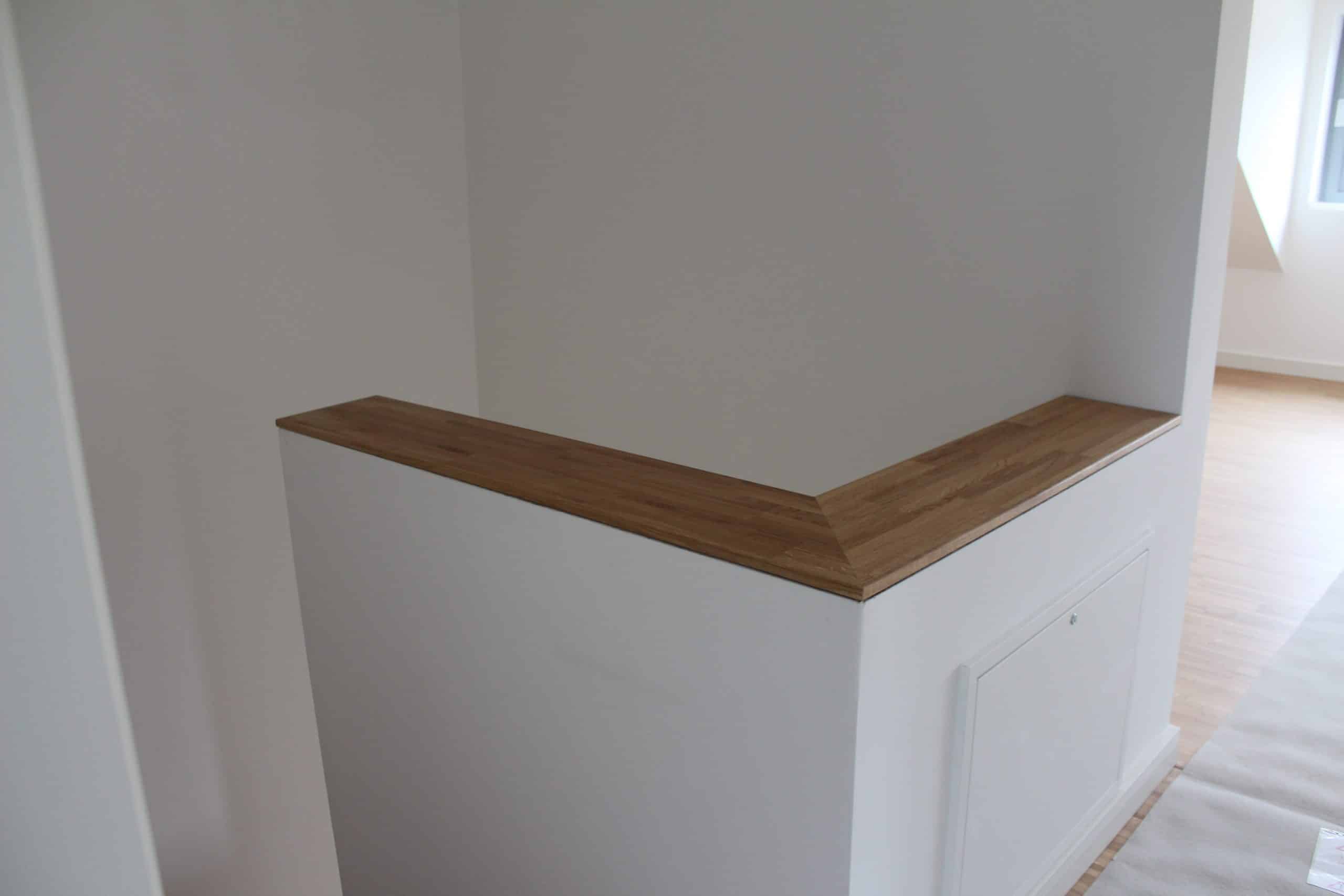 Ein heller Raum mit weißen Wänden und einem Holzregal an einer Ecke. Der Boden ist aus hellem Holz, und der Raum wirkt modern und einladend.