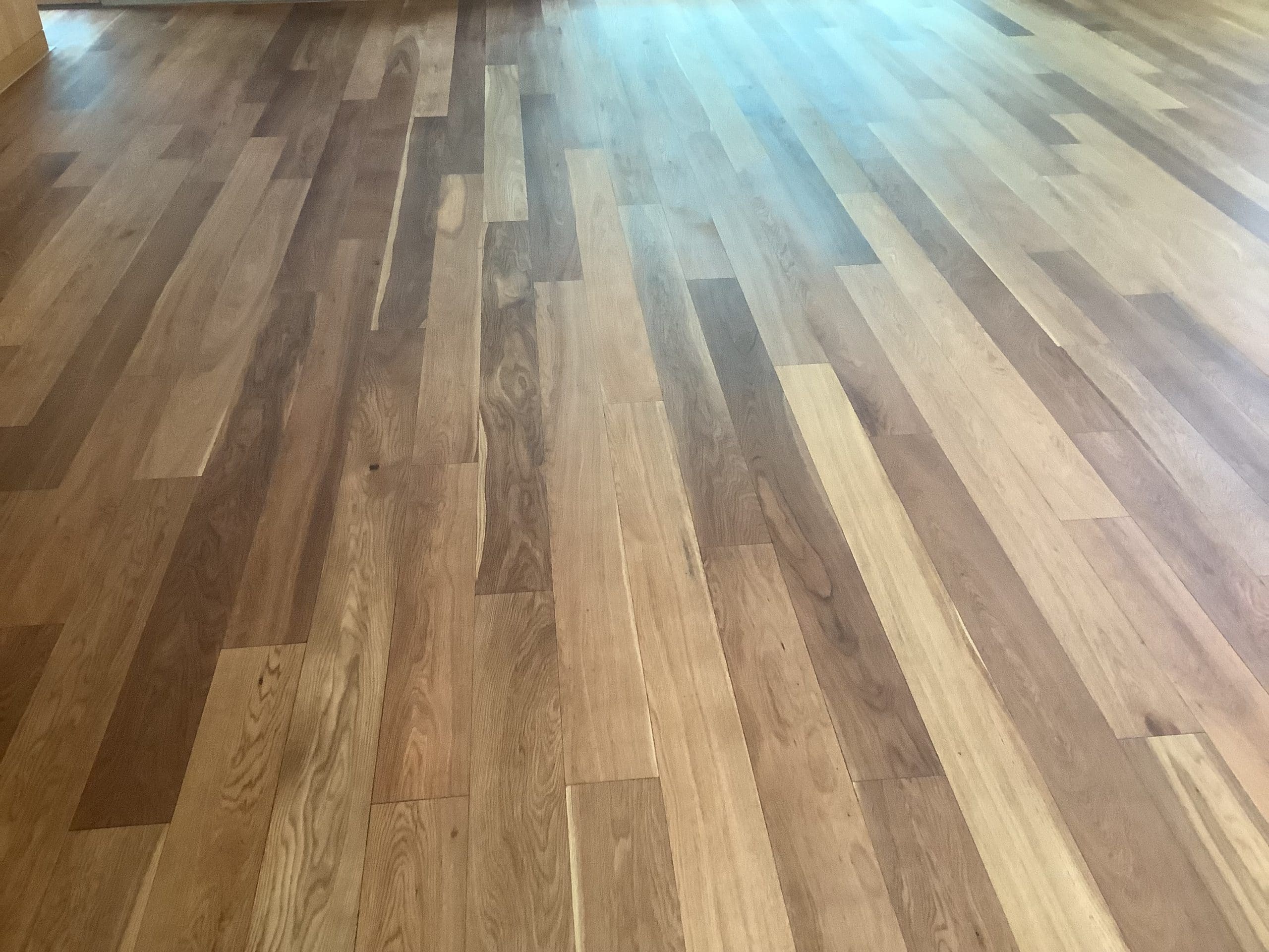 Ein heller Holzboden mit verschiedenen Holzarten, der in einem Raum verlegt ist. Die Dielen zeigen eine natürliche Farbvariation und Maserung.