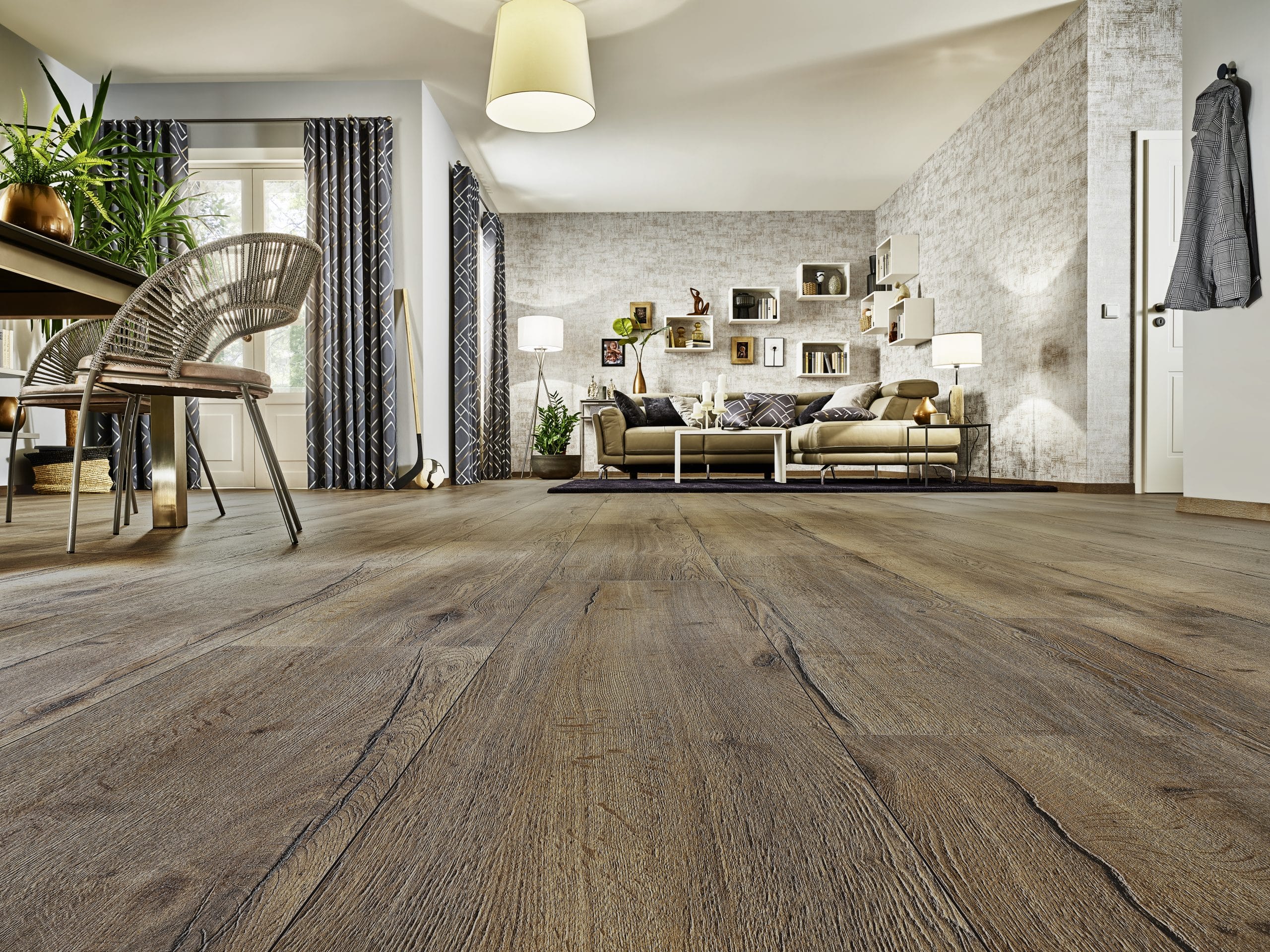 Ein modern eingerichteter Wohnraum mit Holzfußboden, einem großen Sofa, einem Tisch mit einem Stuhl, Pflanzen und dekorativen Elementen an den Wänden.