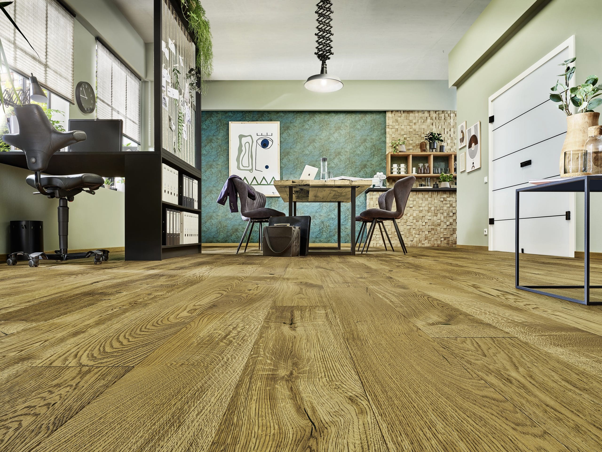 Moderne Büroumgebung mit Holzfußboden, einem Schreibtisch, einem ergonomischen Stuhl und Pflanzen. An der Wand hängen Bilder, und ein Tisch mit Stühlen steht im Vordergrund. Die Wände sind in sanften Farben gehalten.
