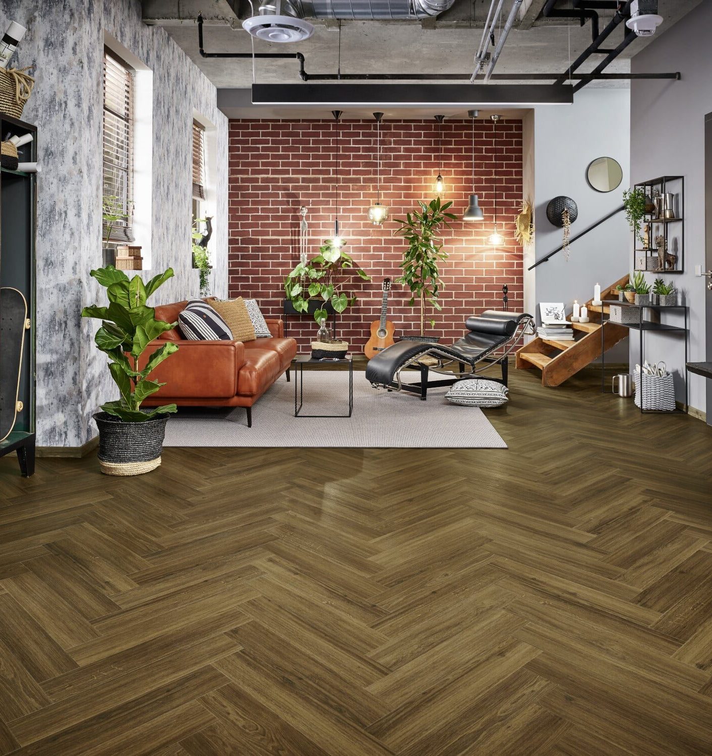 Ein modernes Wohnzimmer mit einer Kombination aus einem braunen Ledersofa, einem schwarzen Lounge-Stuhl und einem Holztisch. Die Wände sind teilweise mit Backstein und teilweise mit einem strukturierten Anstrich versehen. Pflanzen und dekorative Elemente schaffen eine einladende Atmosphäre, während der Boden in Fischgrätmuster verlegt ist.